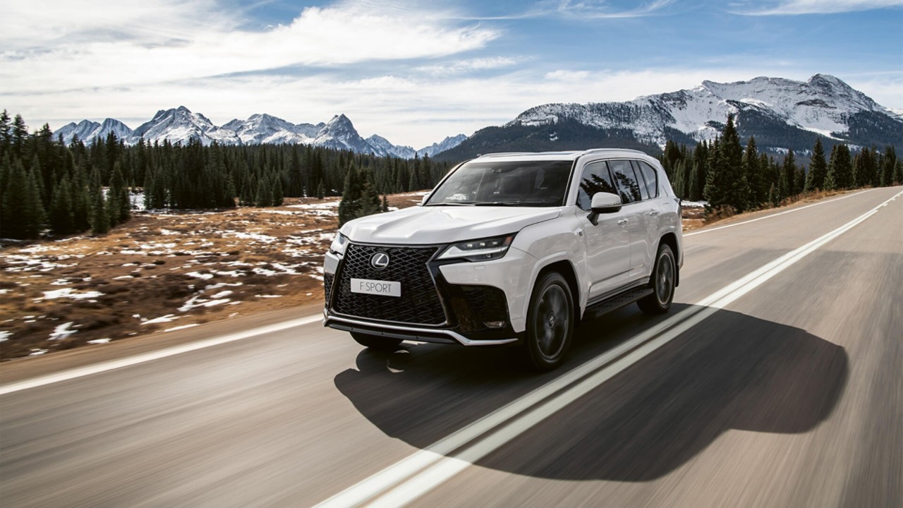 A Lexus LX driving on a road with mountains in the background 
