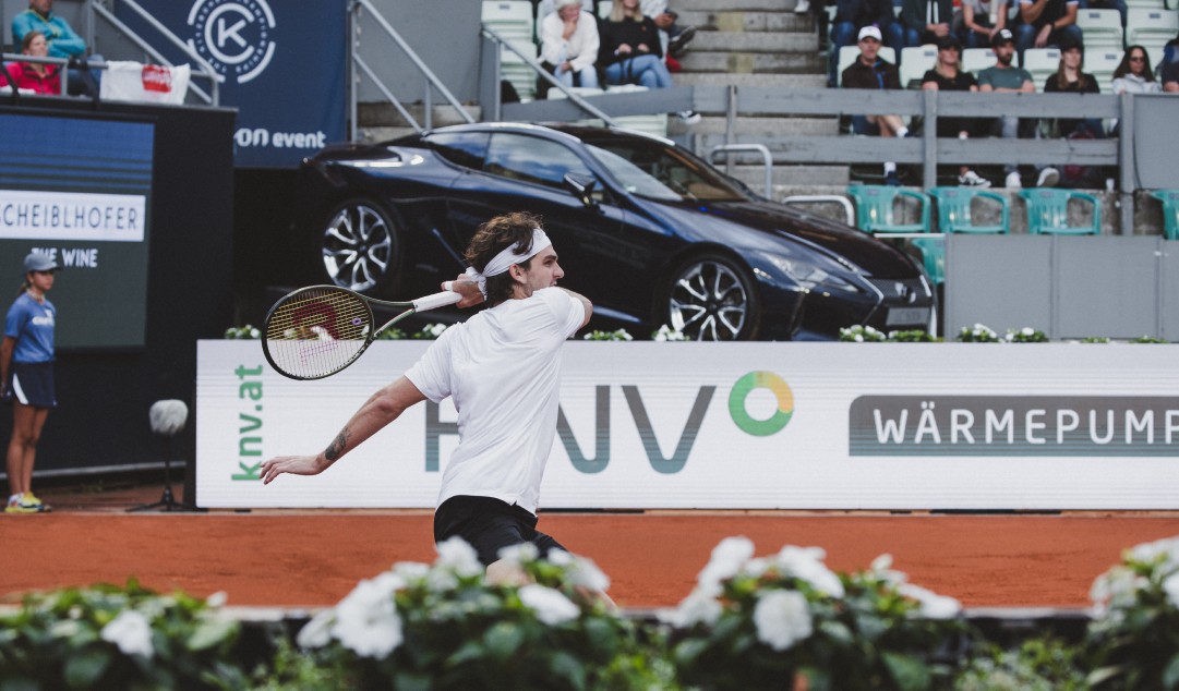 A tennis player on a court with a Lexus in the background
