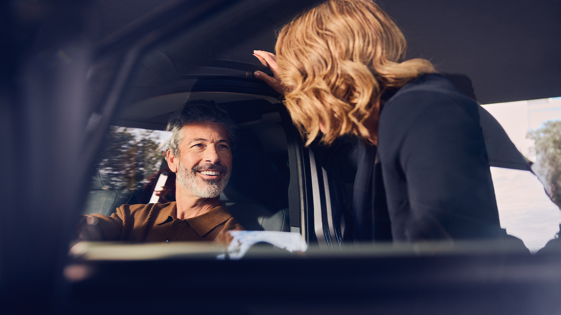 A driver smiling at someone stood in the doorway of a parked Lexus